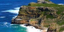 Grassy, rugged cliffs rise out of the crashing waves at Cape of Good Hope Nature Reserve, Cape Town, South Africa